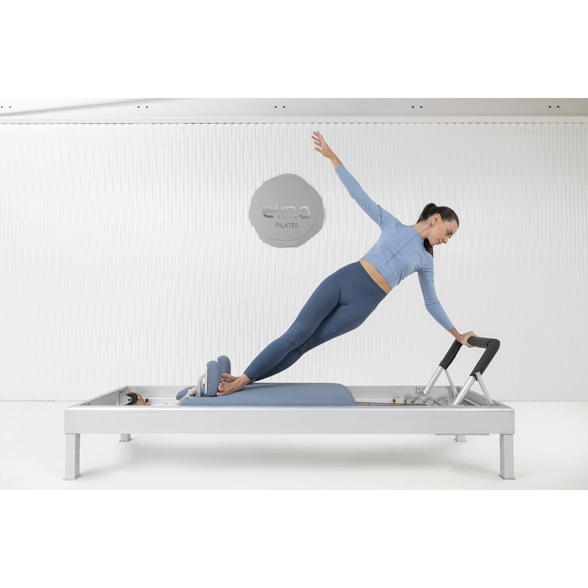 A Pilates practitioner performing a core-strengthening exercise on the Elina Pilates Classic Aluminum Reformer 86″ using natural leather straps.