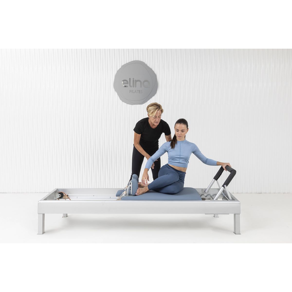 A Pilates practitioner performing a core-strengthening exercise on the Elina Pilates Classic Aluminum Reformer 86″ using natural leather straps.