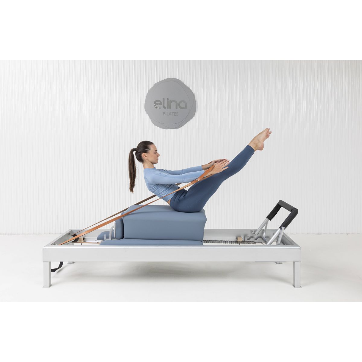 A Pilates practitioner performing a core-strengthening exercise on the Elina Pilates Classic Aluminum Reformer 86″ using natural leather straps.
