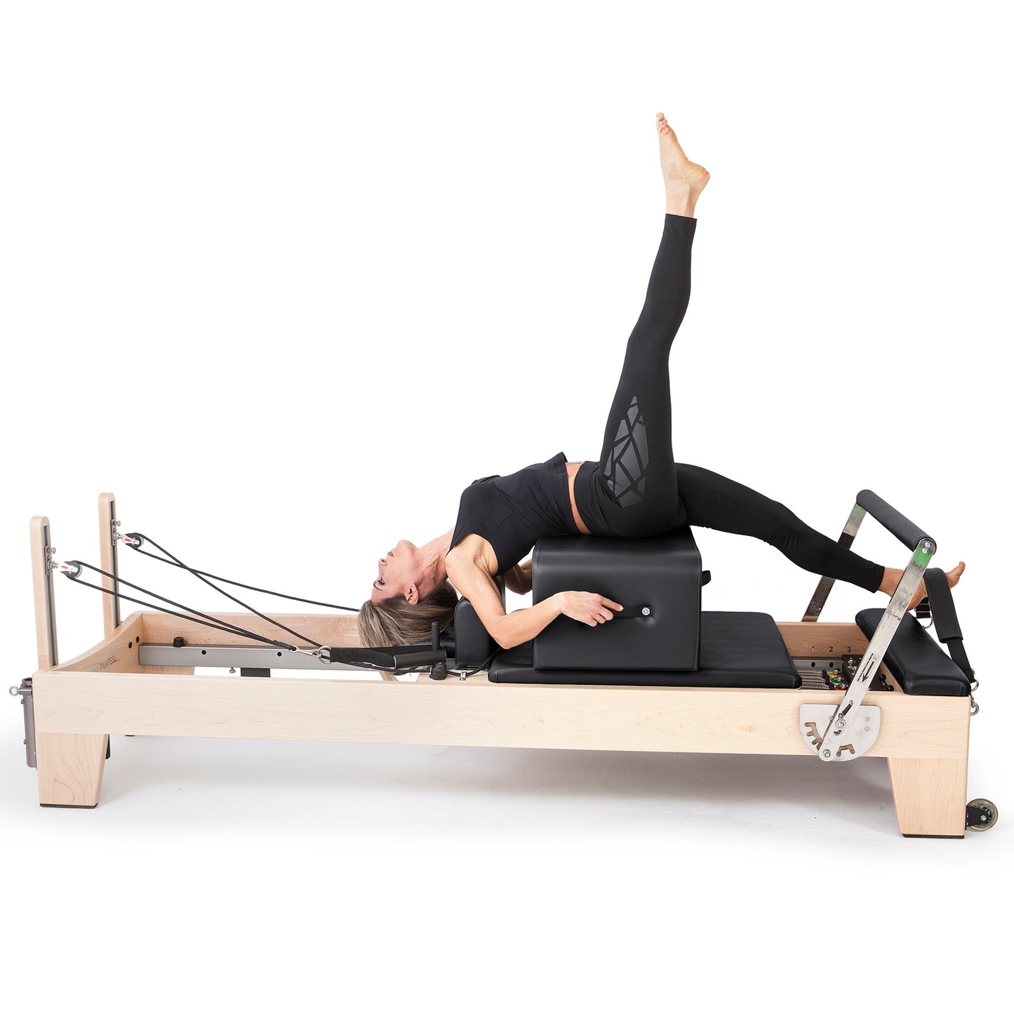 User doing leg strengthening Pilates workout using adjustable footbar and springs on Elina Pilates Elite Wood Reformer