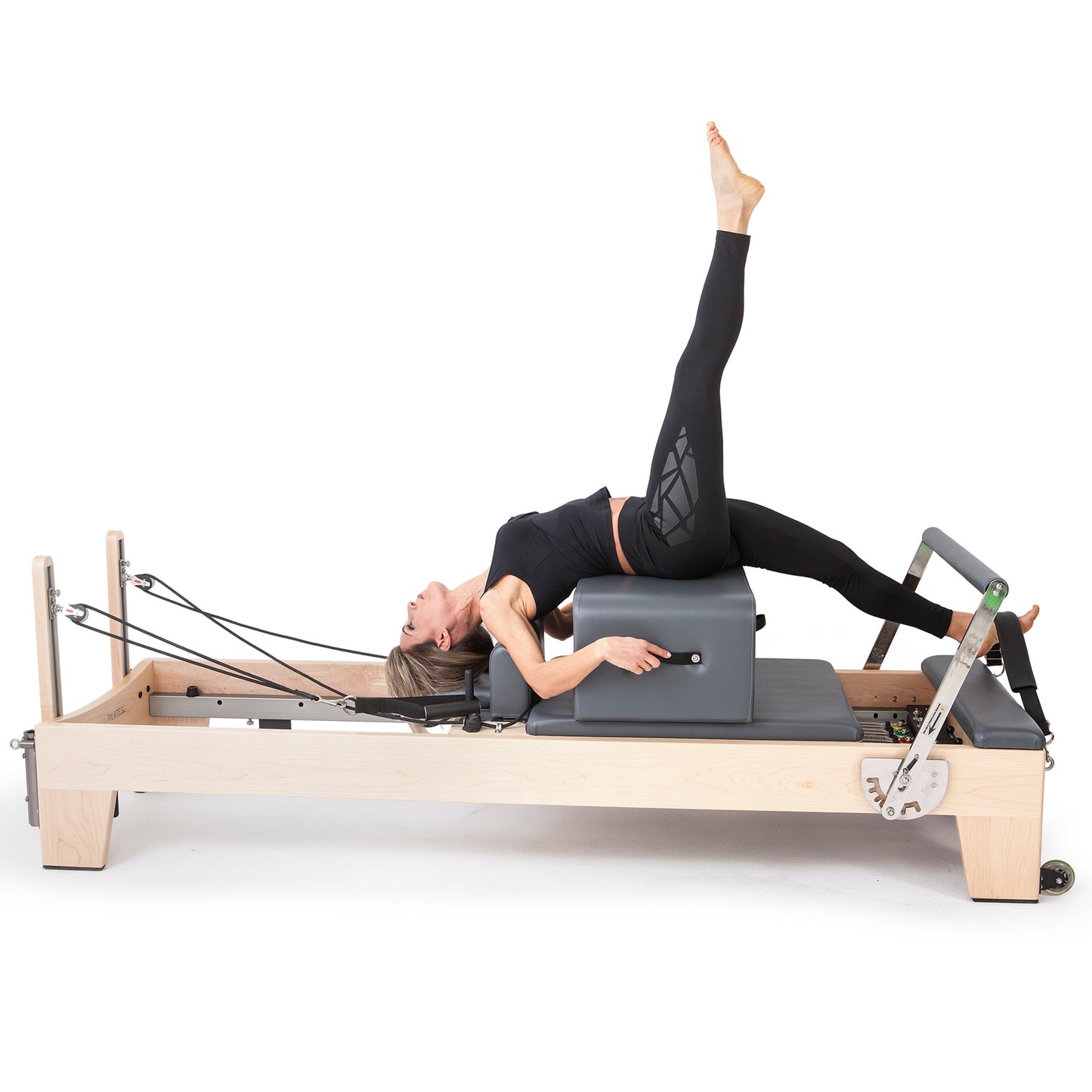 User doing leg strengthening Pilates workout using adjustable footbar and springs on Elina Pilates Elite Wood Reformer