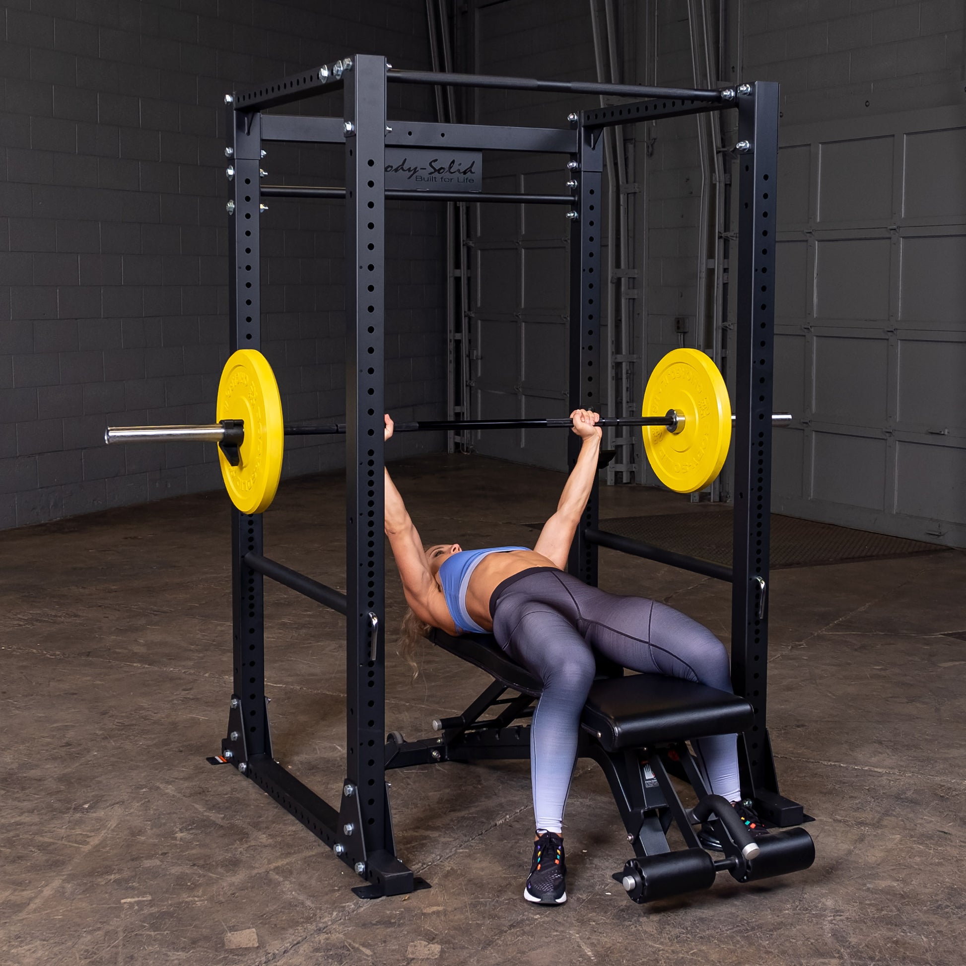 Woman performing bench press on the Body‑Solid GPR400 power rack in home gym