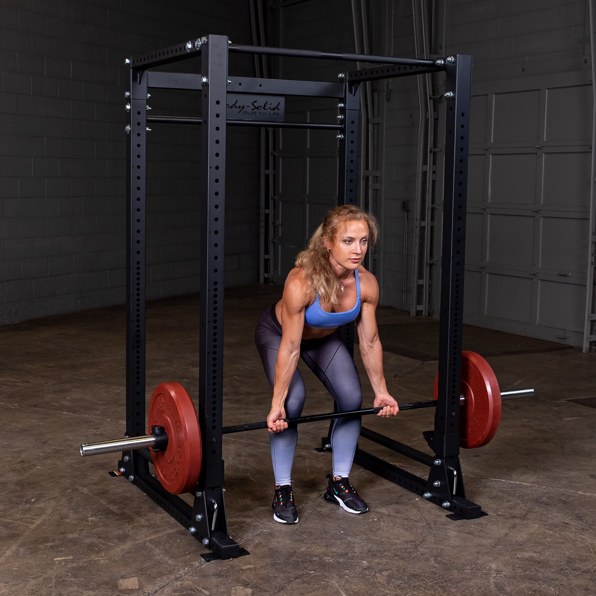 Woman performing bench press on the Body‑Solid GPR400 power rack with wide walk in opening in home gym