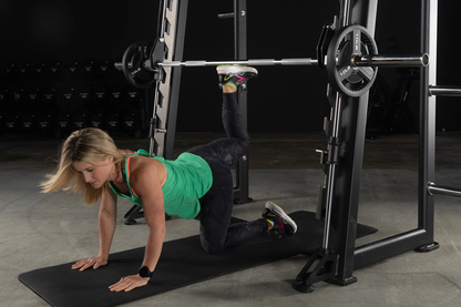 User performing glute kickbacks on the XMark Commercial Smith Machine with steel frame and guide rods